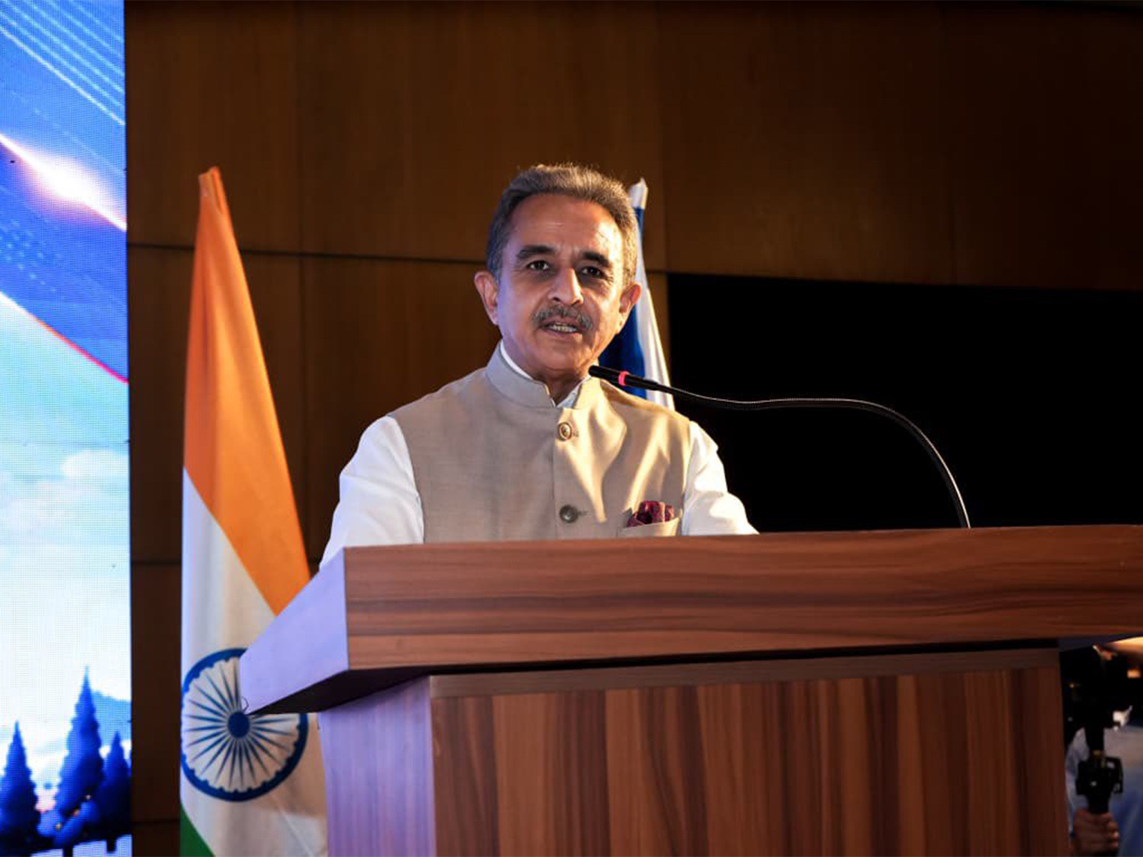 Kirtivardhan Singh speaking at a wooden podium with the Indian flag beside him