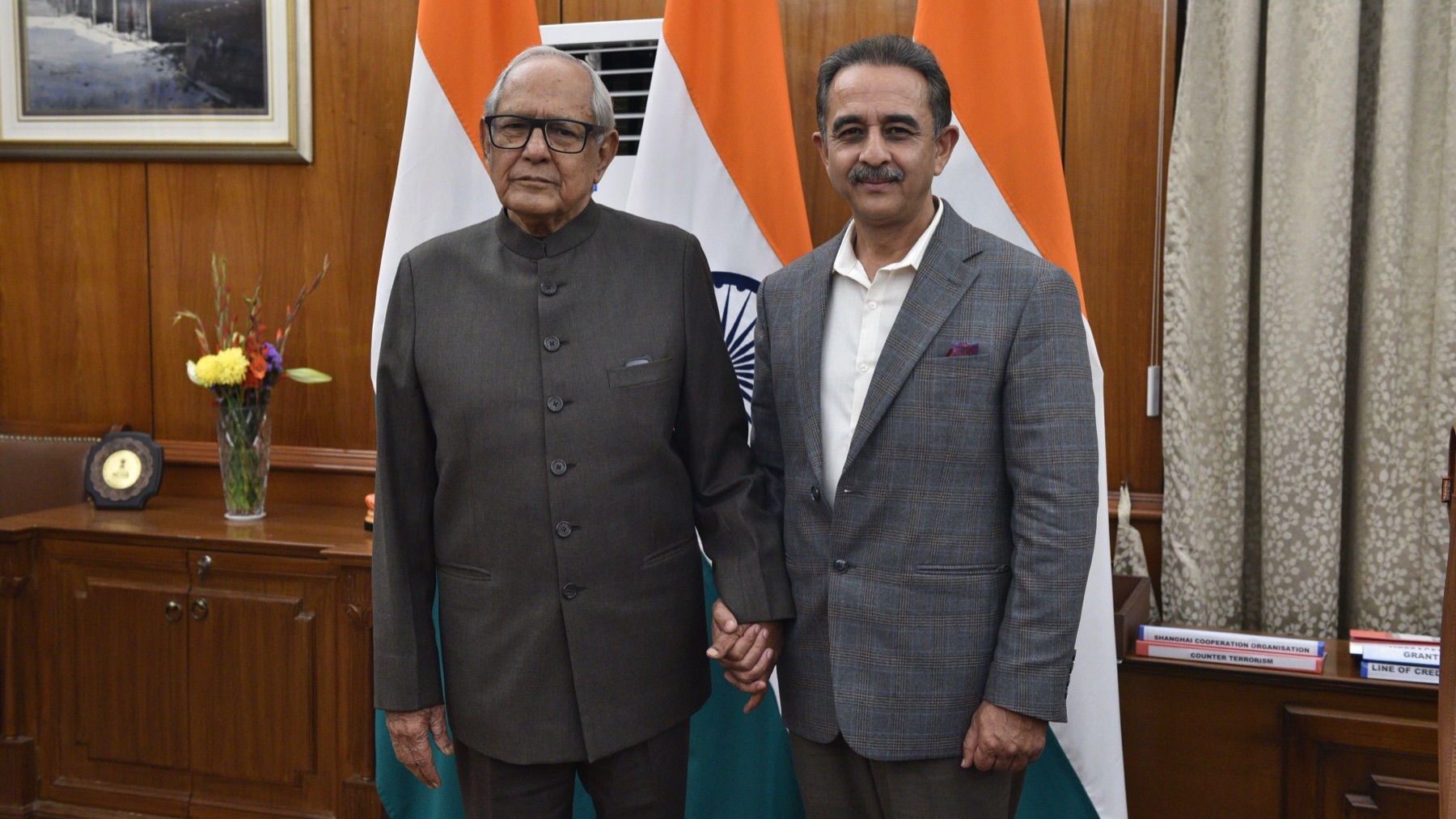 Kirtivardhan Singh standing hand in hand with an elderly man in an office with Indian flags